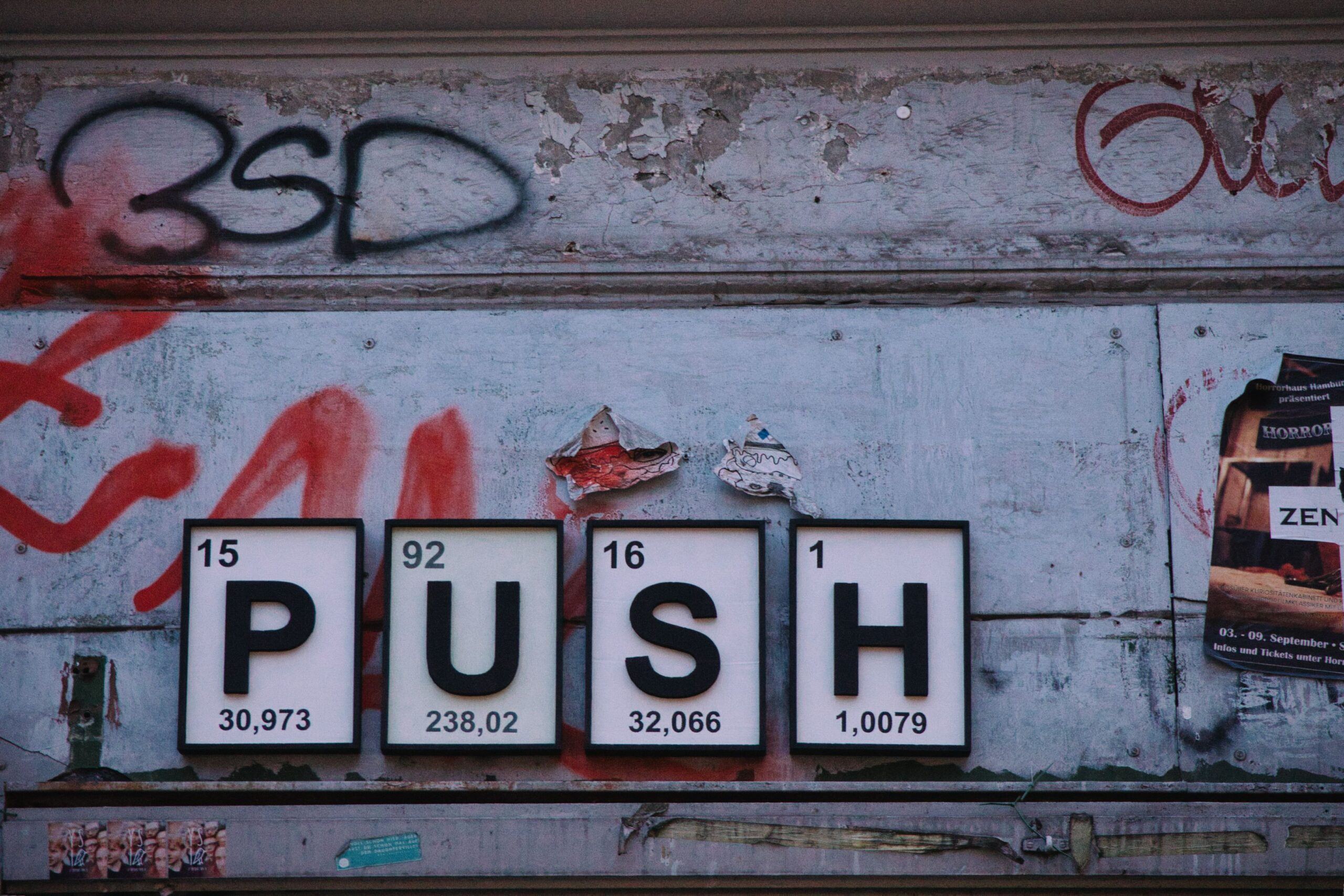 A graffiti'd wall with the chemical symbols from the periodic table used to spell out "PUSH."